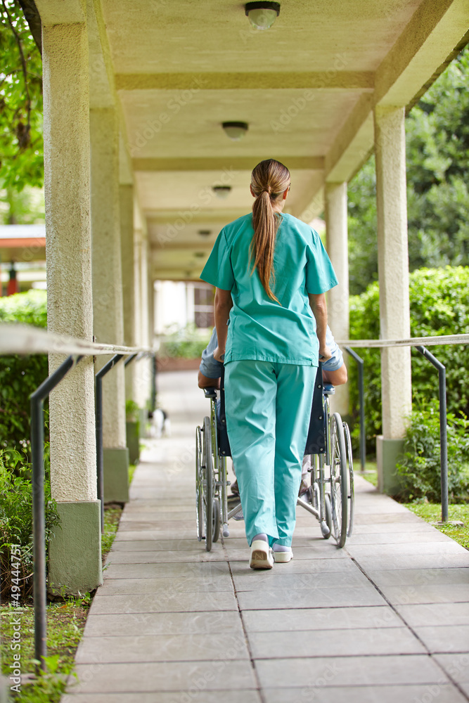 Krankenschwester schiebt Rollstuhl im Pflegeheim