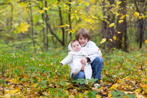 Brother holding baby sister in white jackets with yellow trees
