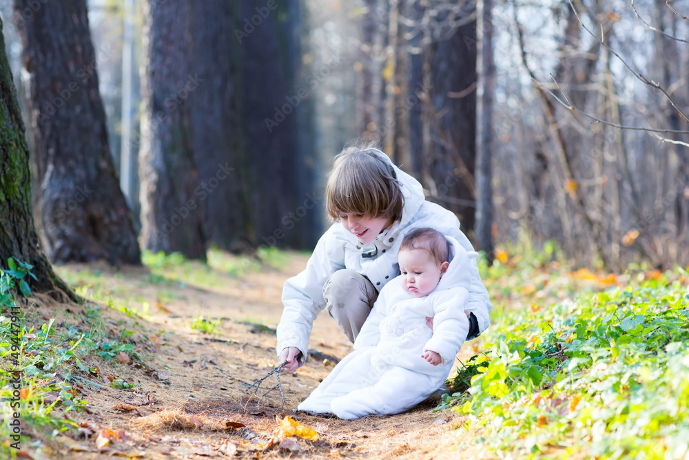Brother and baby sister in white jackets playing in a park Brother and baby sister in white jackets playing in a park