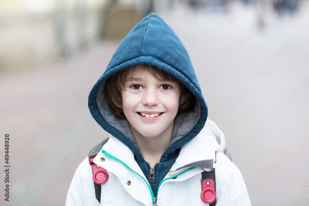 Happy school boy walking on street with backpack on cold day