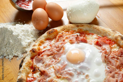 Typical Italian Pizza, ingredients in background on wood table