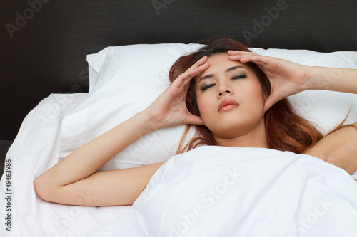 sick woman on bed massaging her head to relieve pain or stress