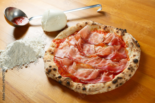 Typical Italian Pizza, ingredients in background on wood table