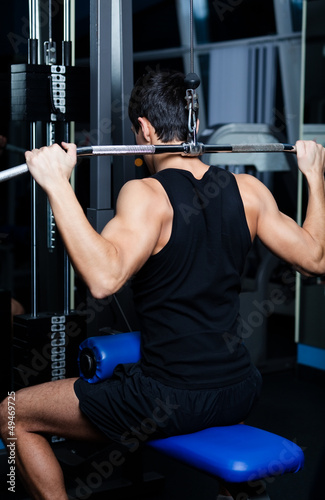 Athletic young man works out on training apparatus in gym class