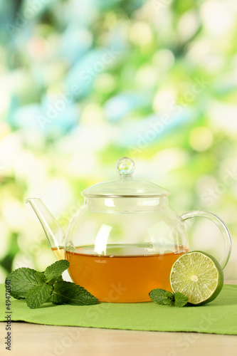 Teapot with mint and lime on table on bright background