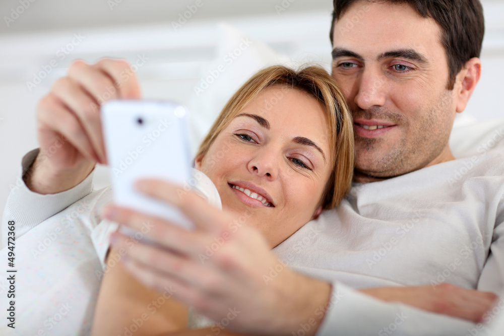 Fototapeta premium Couple laying in sofa and using spartphone