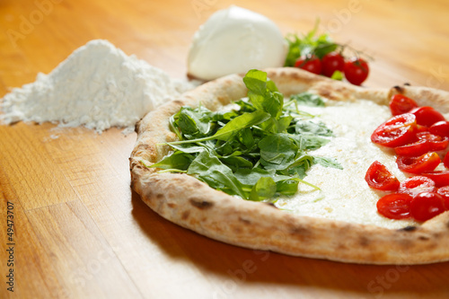Typical Italian Pizza, ingredients in background on wood table