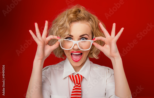 Surprised woman looking you above eyeglasses, isolated on red photo