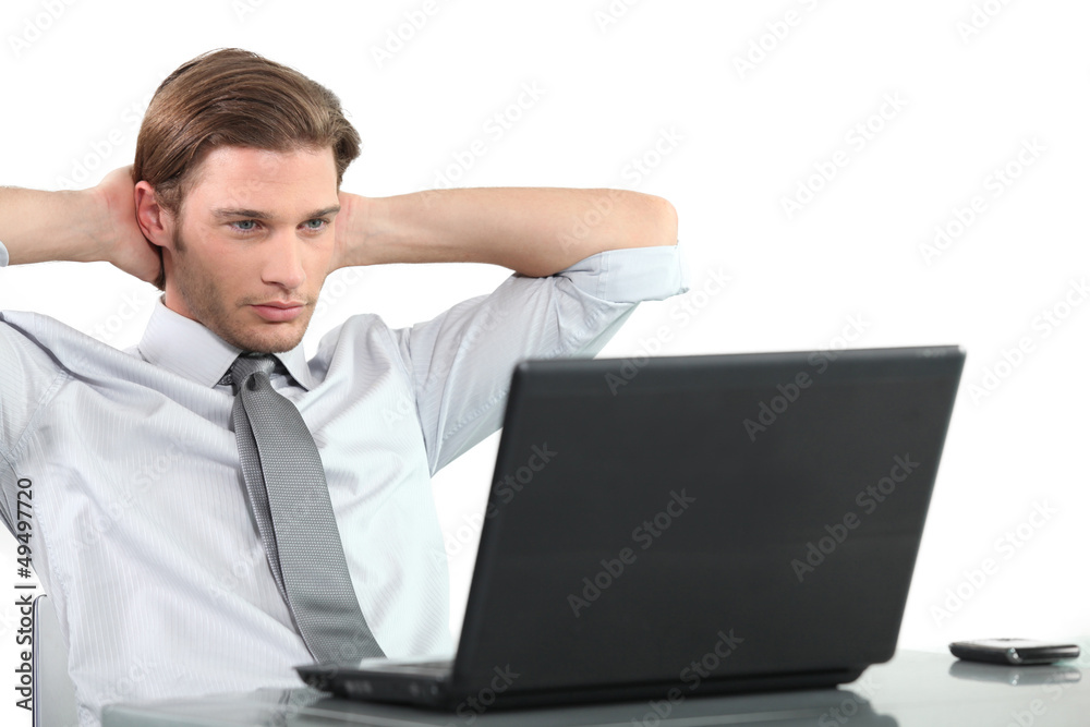 Young businessman at laptop with arms behind head. Young businessman at laptop with arms behind head.