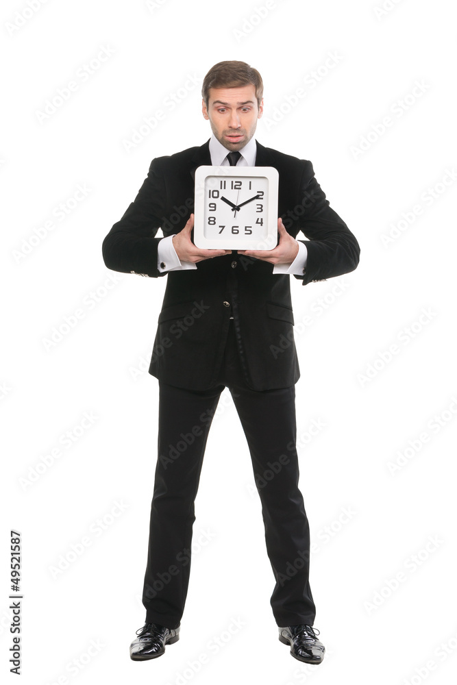 Upset young man holding a wall clock in hand full length on whi Upset young man holding a wall clock in hand full length on whi