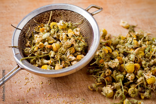 dried chamomile flowers with colander on wooden plate