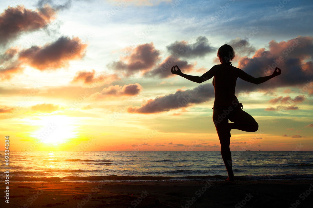 Young woman practicing yoga on the beach during the sunset