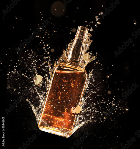 Concept of liquor splashing around bottle on black background photo