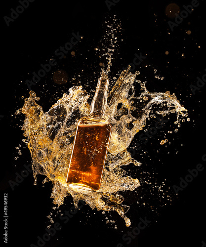 Concept of liquor splashing around bottle on black background photo