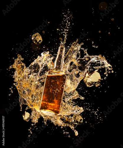Concept of liquor splashing around bottle on black background photo