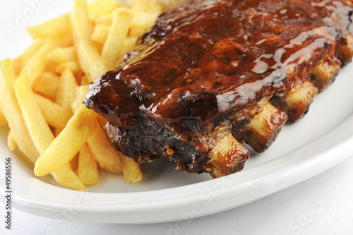 Grilled juicy barbecue pork ribs in a white plate with fries.