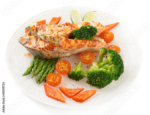 Salmon steak with vegetables in plate isolated on white