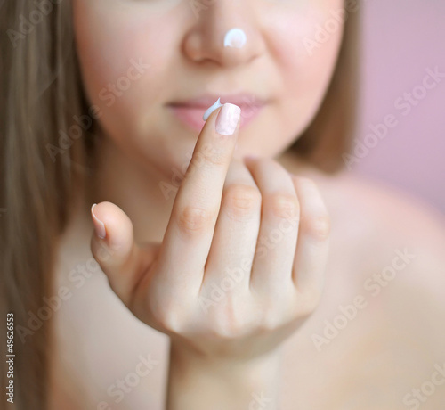 Beautiful woman with cream on her nose. Focus is on a finger