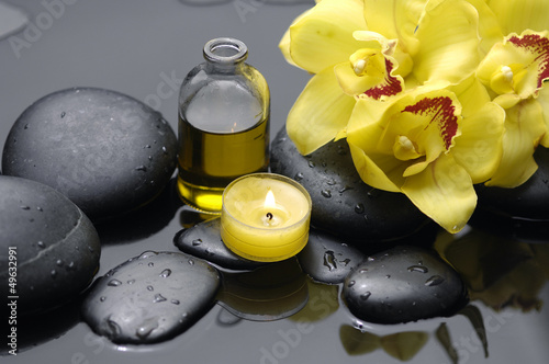 Yellow orchid with candle and massage oil on therapy stones