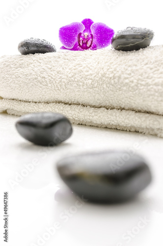 Massage stones and violet orchid flower on a towel