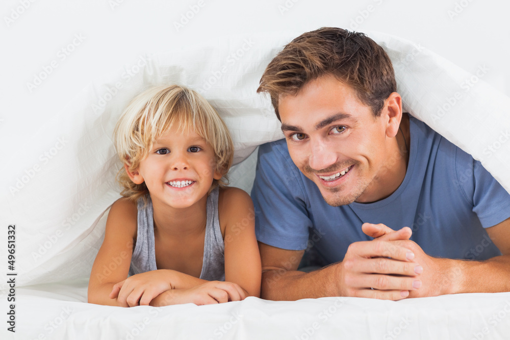 Father and his son lying under the duvet Father and his son lying under the duvet