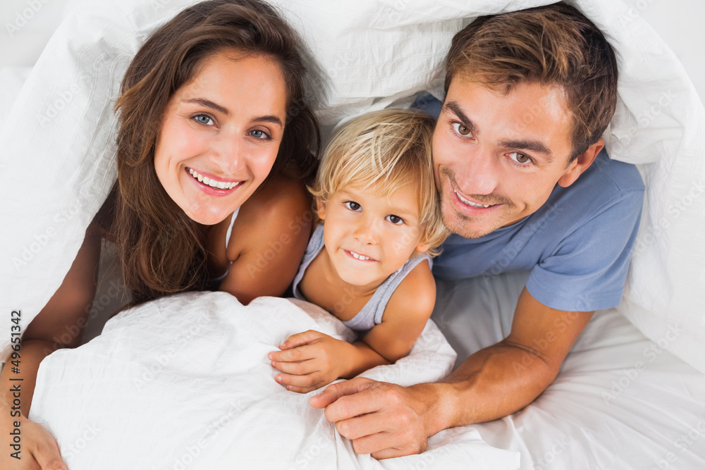 Family smiling under the duvet on the bed