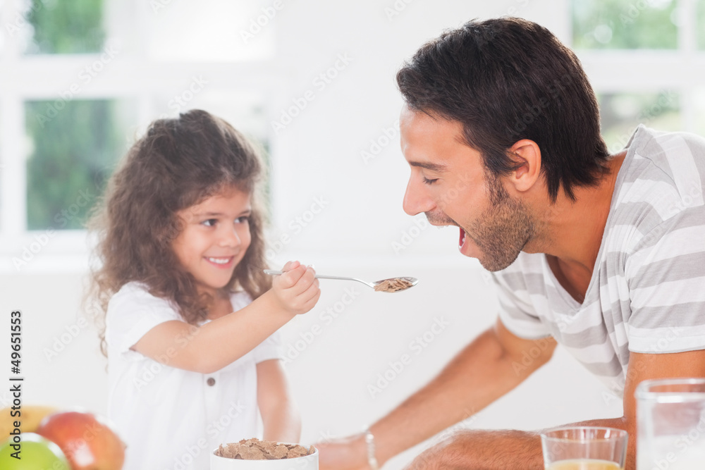 Little girl feeding cereal to father Little girl feeding cereal to father