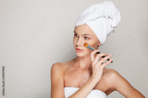 Beautiful young woman in bath towel. Applying makeup