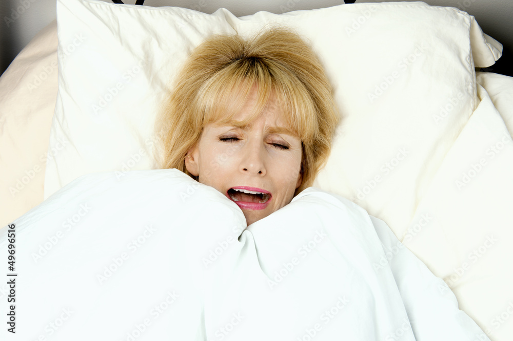 Woman pulling blanket to her face in fear Woman pulling blanket to her face in fear