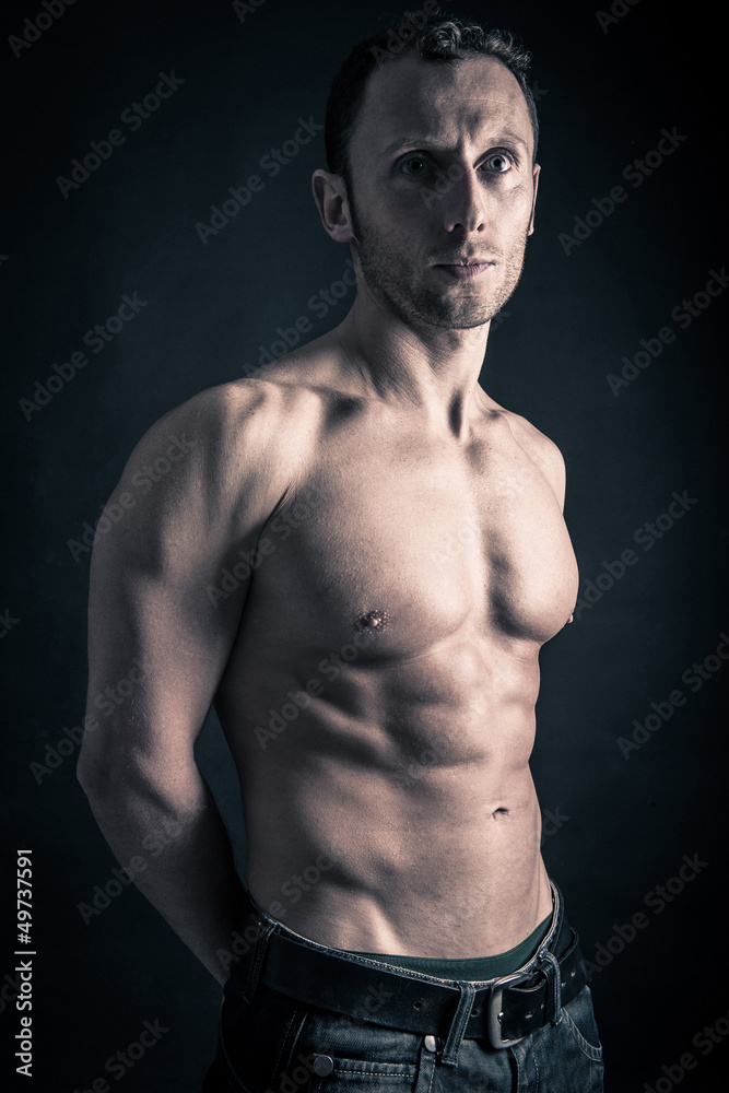 Confident young man shirtless portrait against black background.
