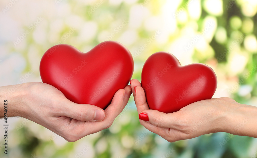 Red hearts in woman and man hands, on green background Red hearts in woman and man hands, on green background