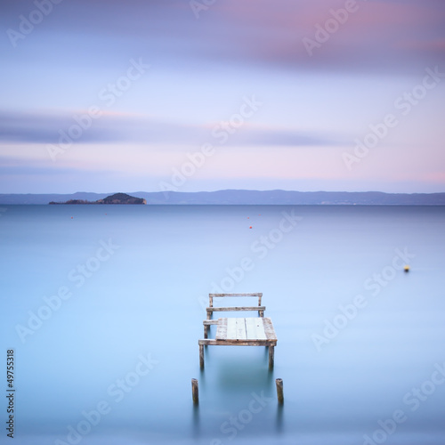 Wooden pier or jetty on a blue lake. Hills on background. Italy