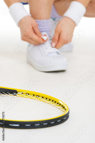 Closeup on tennis racket and tennis player tying shoelaces