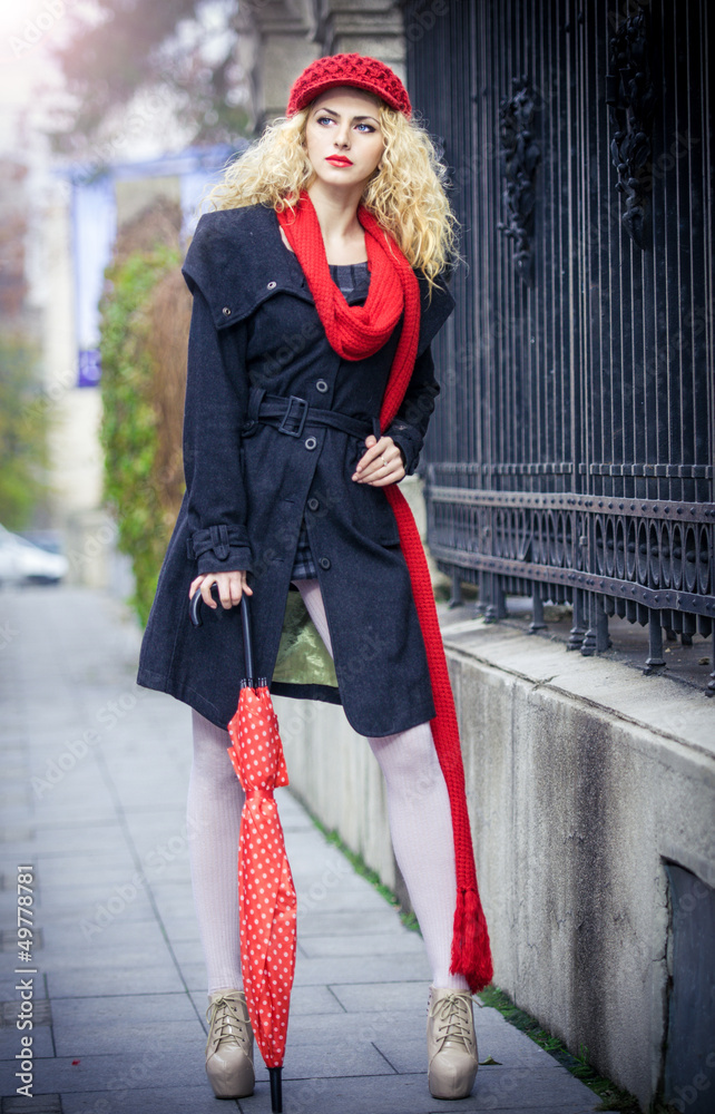 Beautiful fashionable young girl with red umbrella in the street