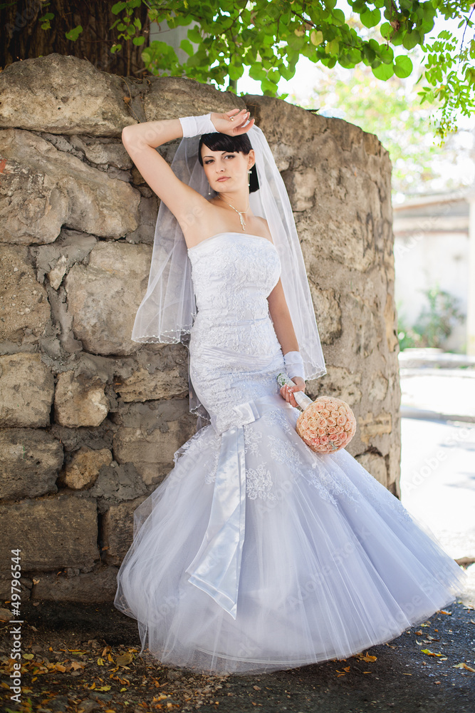 bride portrait near the wall in white dress with bouquet