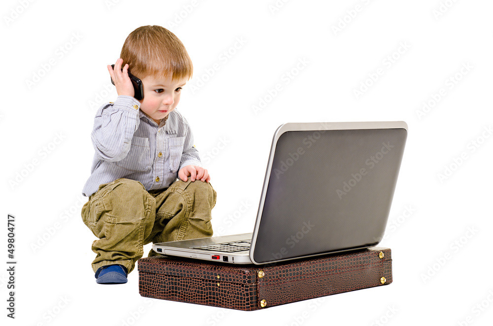 Cute little boy speaks on a mobile phone looking at laptop Cute little boy speaks on a mobile phone looking at laptop