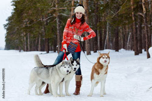 Happy woman playing with siberian husky dogs in winter forest