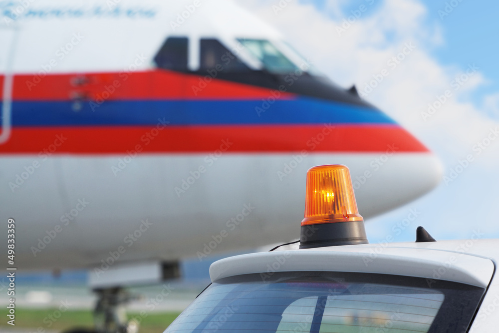 Car with flasher on roof and aircraft at airport