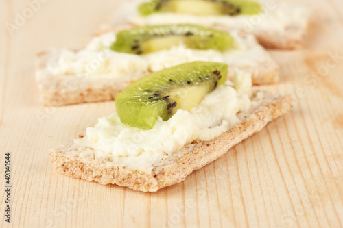 Tasty canapes with cheese and kiwi, on wooden background