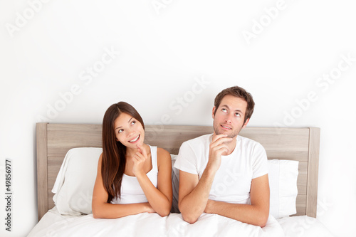 Thinking young couple sitting pensive in bed