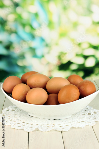Eggs in white bowl on wooden table on natural background