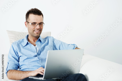 Handsome man in glasses using laptop on sofa