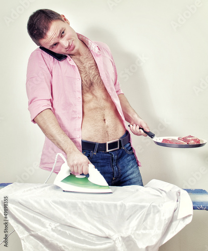 Young man with pan and phone ironing his shirt photo