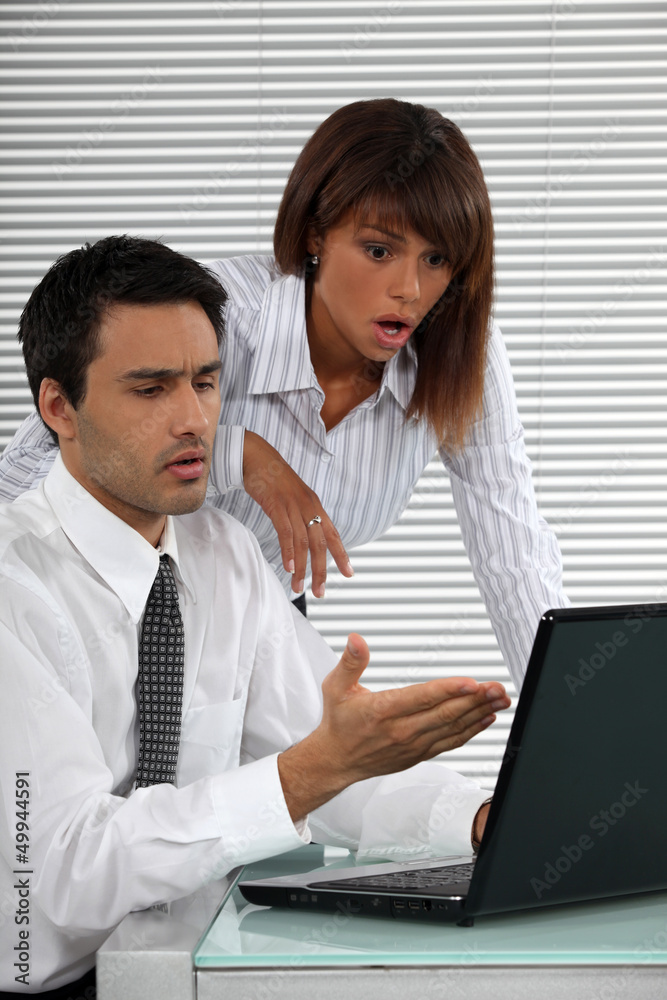 Two businessworkers shocked by laptop screen Two businessworkers shocked by laptop screen