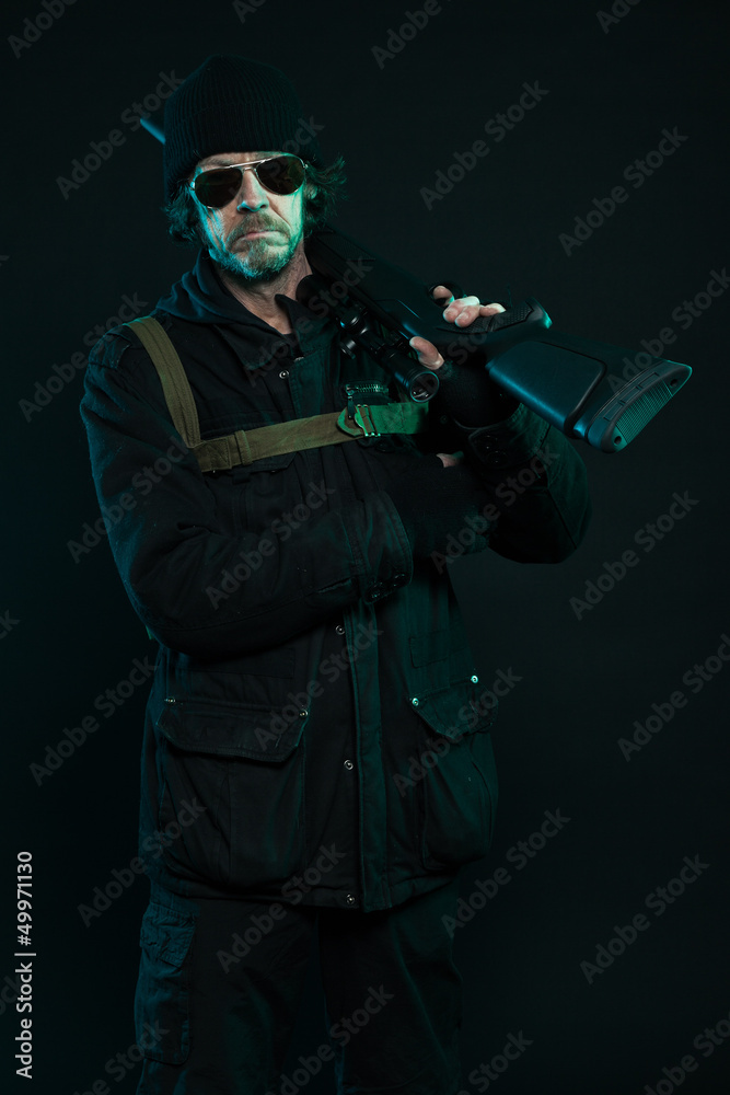 Sniper with beard in black holding gun. Studio shot.