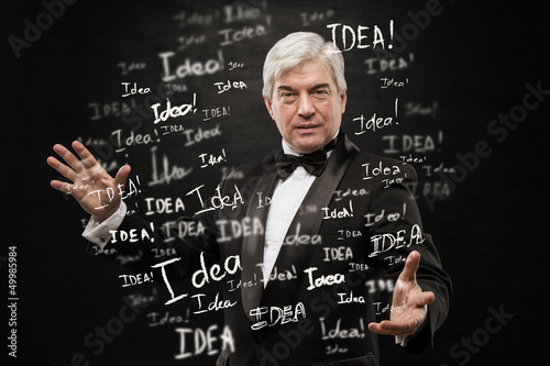 Idea concept. Mature business man standing on black background w