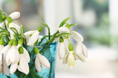 Bouquet of snowdrop flowers in glass vase, on bright background