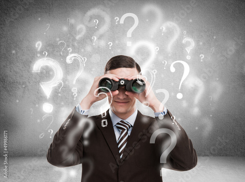 Handsome business man with binoculars and question marks above h photo