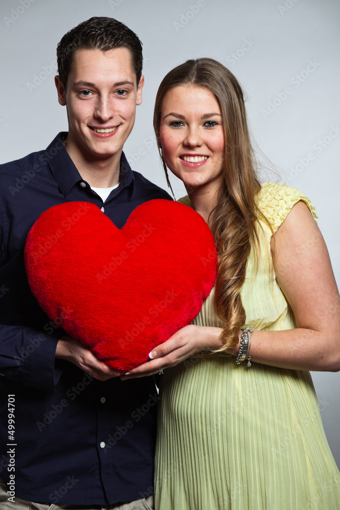 Happy young romantic couple holding red heart. Studio shot.