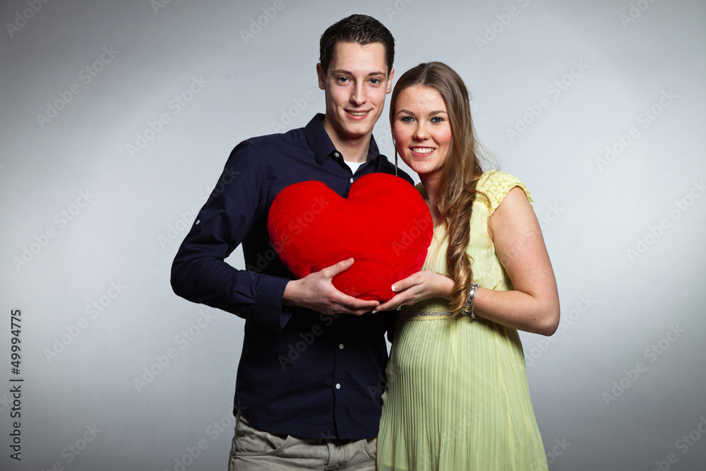 Happy young romantic couple holding red heart. Studio shot.